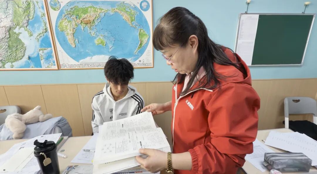 老师在教室内逐个翻查学生的练习与检测册。往期全日制班教学实拍，非本届艺考班现场。